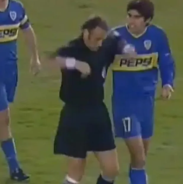 A referee and a soccer player in a blue uniform with the word "PEPSI" on it are standing on a green field.
