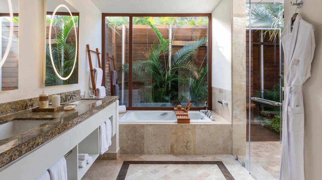 Bathroom at Fairmont Mayakoba hotel with a bathtub by a large window overlooking lush greenery.