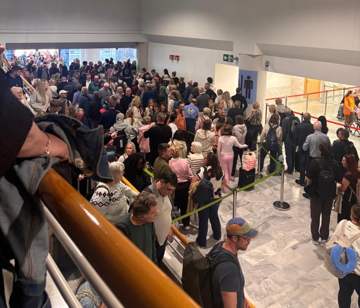 A large crowd of people waiting in a roped-off queue inside an airport or building.