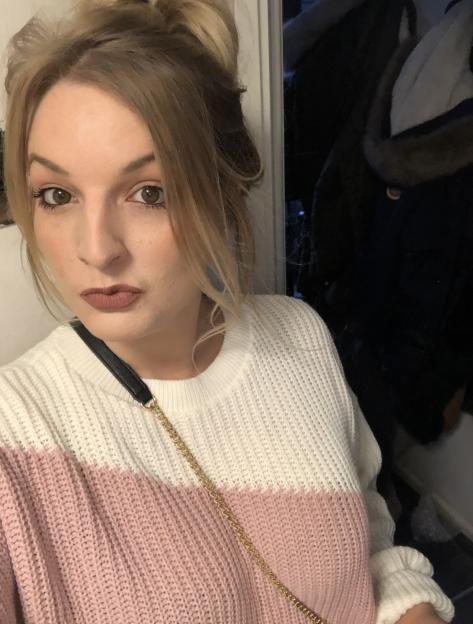 A woman with blonde hair in a messy bun and a pink and white sweater looks at the camera.