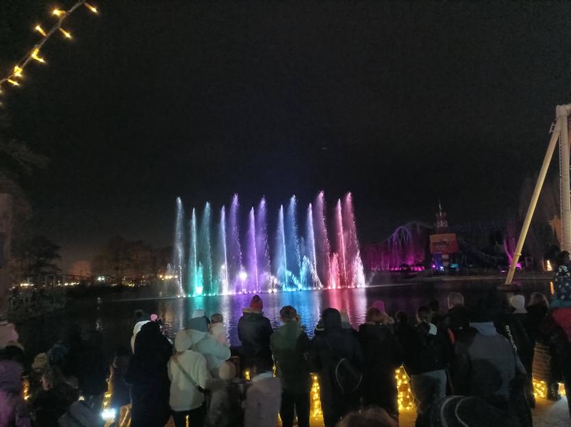 Attendees at Drayton Manor Theme Park watch an end-of-day light show featuring colorful fountains on a lake.
