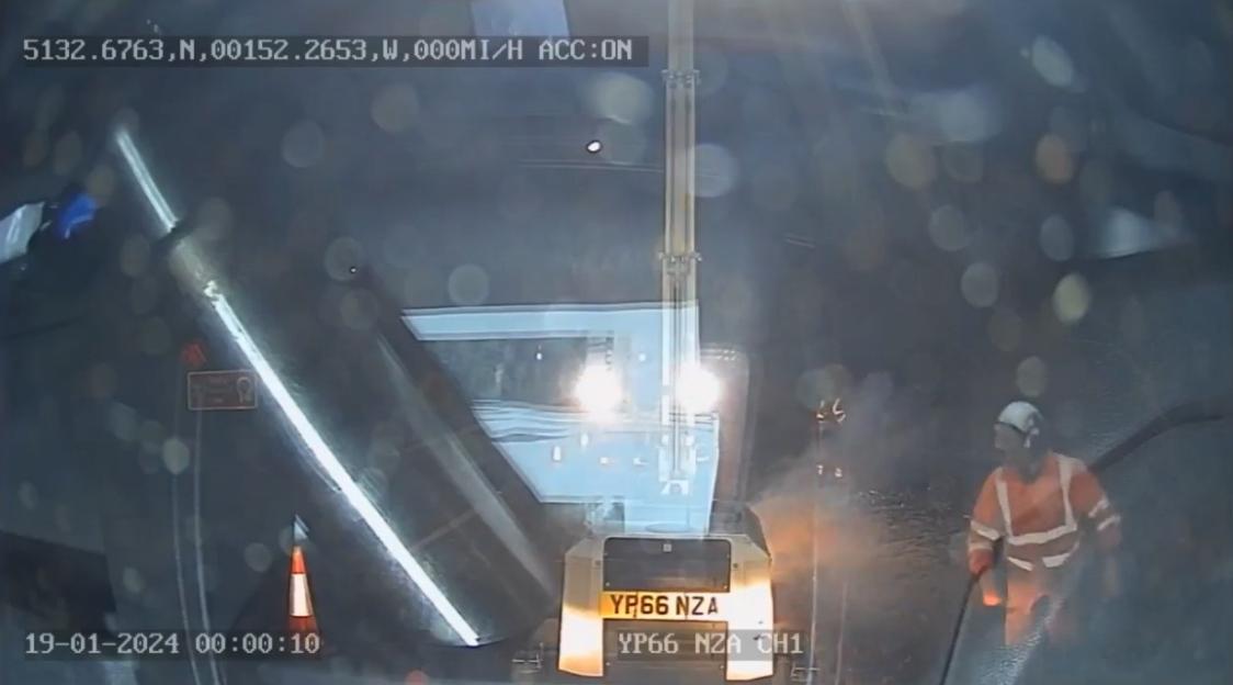 Dashcam footage of road maintenance worker in an orange uniform and hard hat next to a vehicle with the license plate YP66 NZA.