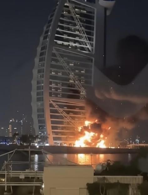 A large fire burns next to the Burj Al Arab hotel in Dubai at night.