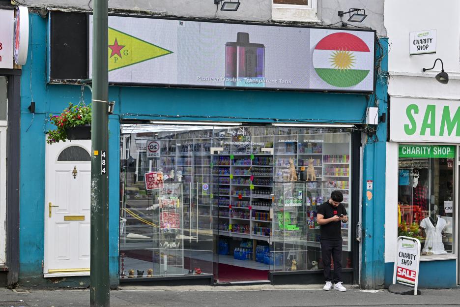 A man looks at his phone outside a vape shop with a digital sign above it.