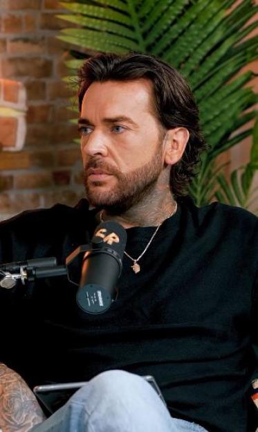 Pete Wicks looking away from the camera while seated next to a microphone.