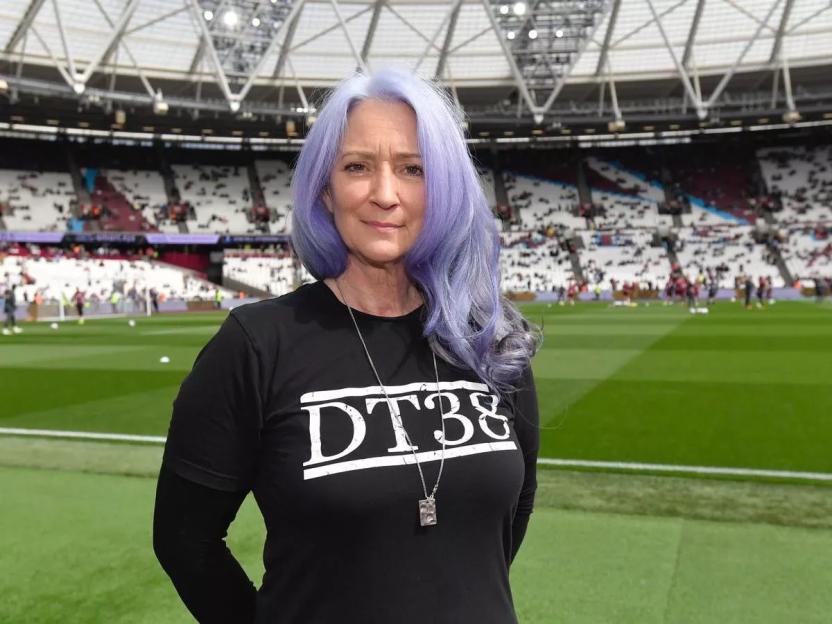 Woman with lavender hair wearing a black "DT38" shirt in a stadium.