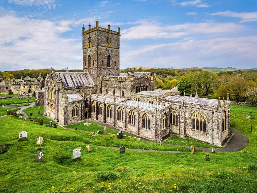 St Davids Cathedral, a large stone church with a square bell tower, surrounded by green grass and gravestones.