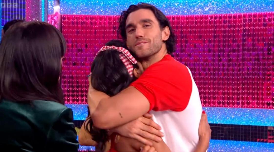 A man in a red and white shirt hugs a woman wearing a red and white checkered headband.
