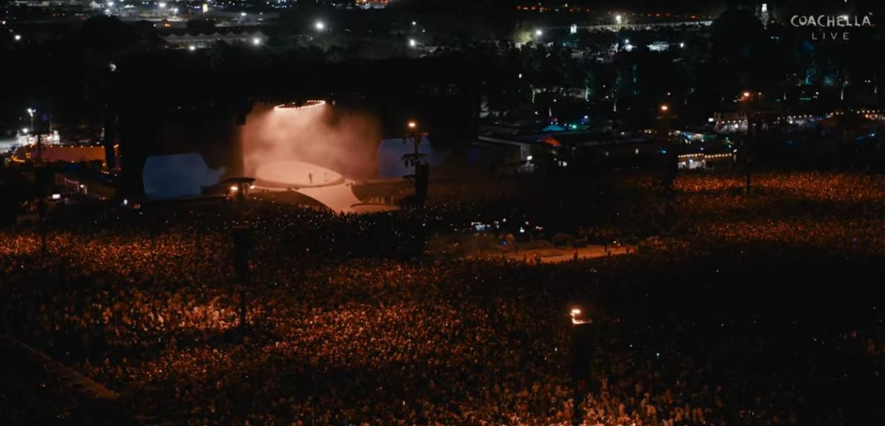 Justin Bieber performing on stage at Coachella, illuminated by a spotlight, in front of a massive crowd at night.