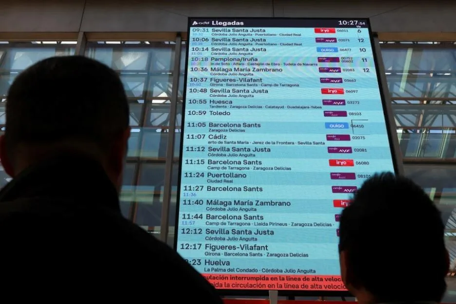 People check an arrivals information screen at a train station.