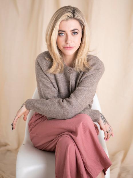 Aurora Grace, a 31-year-old sex surrogate, sits on a white chair against a beige backdrop.