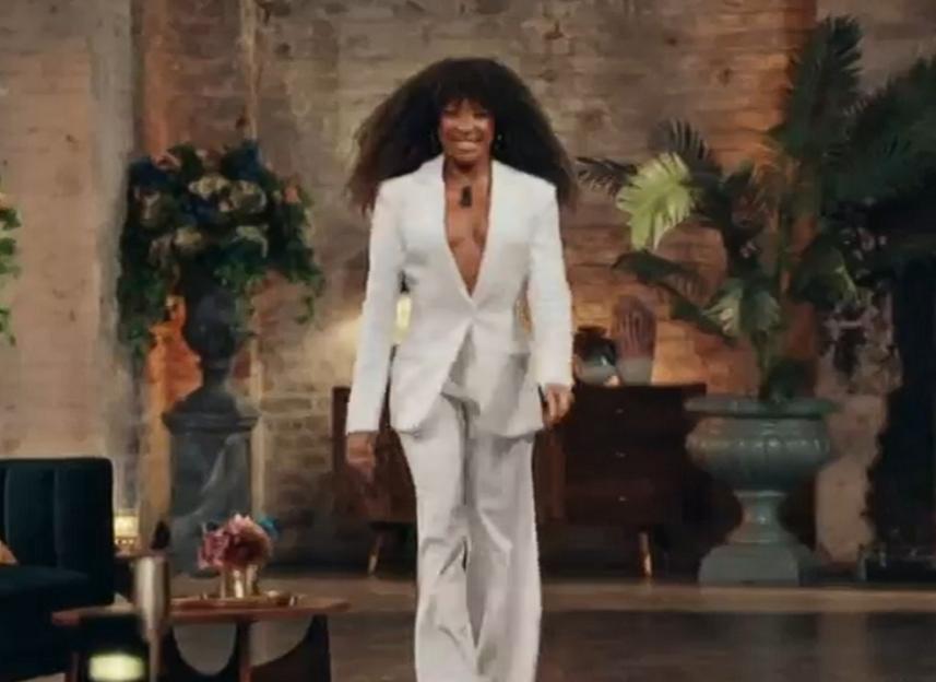 A woman in a white suit walks towards the camera.