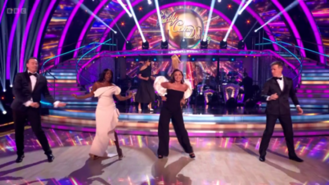 Three women and two men dancing on a stage in formal wear.