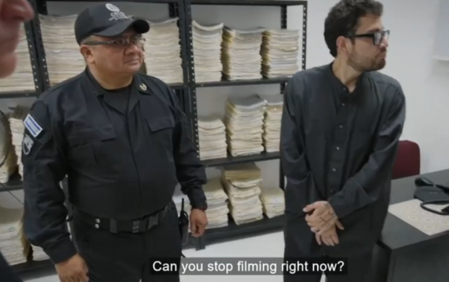 A police officer and a man in a black shirt standing in a room with shelves full of documents.
