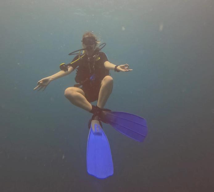 A female diver with blue fins meditates underwater.