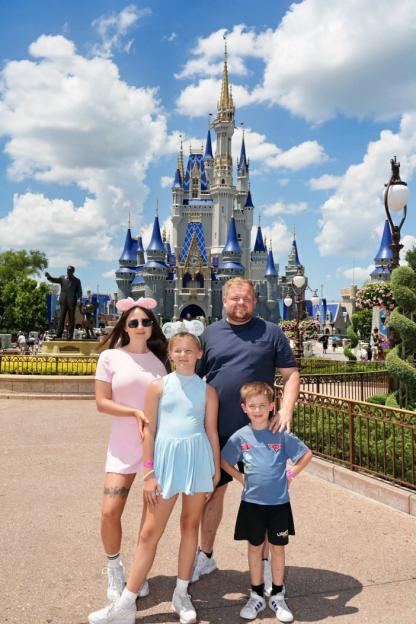 Family of four at Disney World, posing in front of Cinderella Castle.