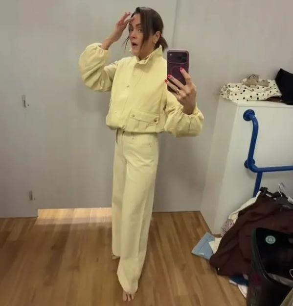 A woman in a fitting room wearing a butter yellow jacket and matching jeans.