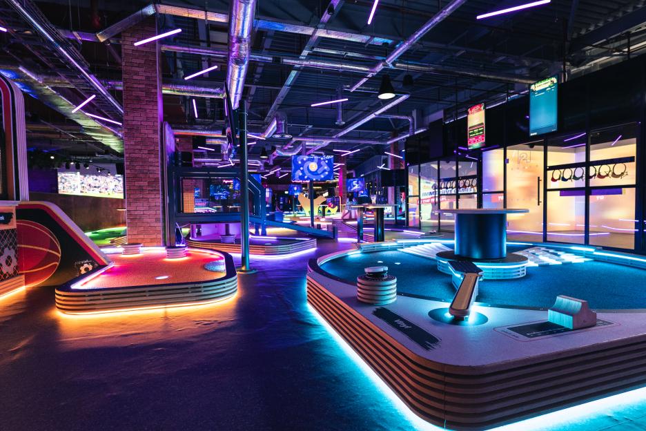 Indoor mini-golf course with vibrant neon lighting.