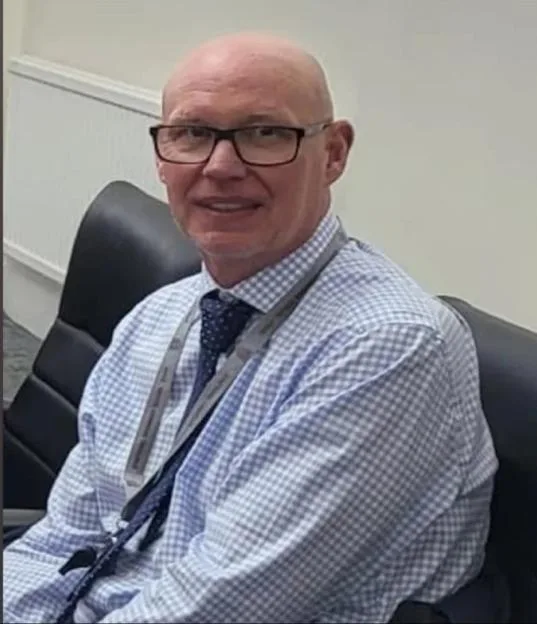Michael Mullins, headteacher of Stretford Grammar School, smiling while sitting in an office.