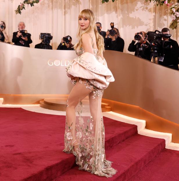Jennifer Lawrence on the red carpet at the Golden Globe Awards, looking over her shoulder at the cameras.