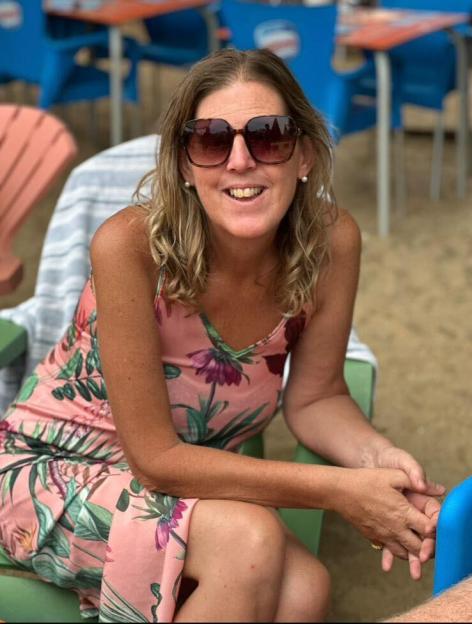 Shona Sibary, 55, sits outdoors in a pink floral dress and sunglasses.