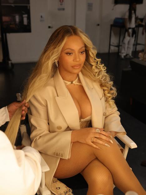 Beyoncé in a light-colored blazer getting her long blonde hair styled.