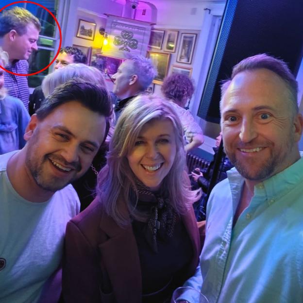 Kate Garraway, Josh Lovatt, and Paul Bartlett posing for a selfie at The Hooligans Gig at the Railway Arms, with Liam Halligan circled in the background.