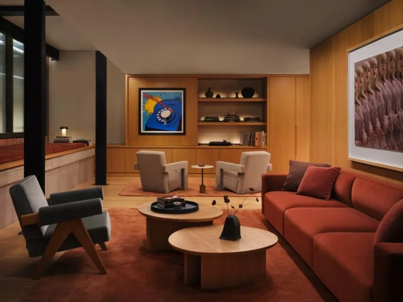 A luxurious living room with a red sofa, armchairs, coffee tables, and a framed painting of Billie Eilish.