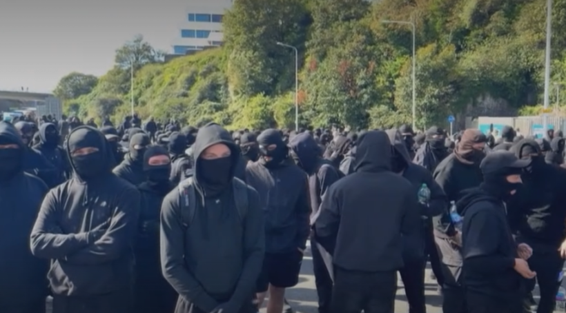 A crowd of people, many wearing black hoodies and balaclavas, gathered for a protest.