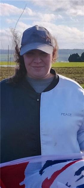 A woman in a blue cap and a jacket that is half black and half light blue with the word "PEACE" on the light blue side, smiling.