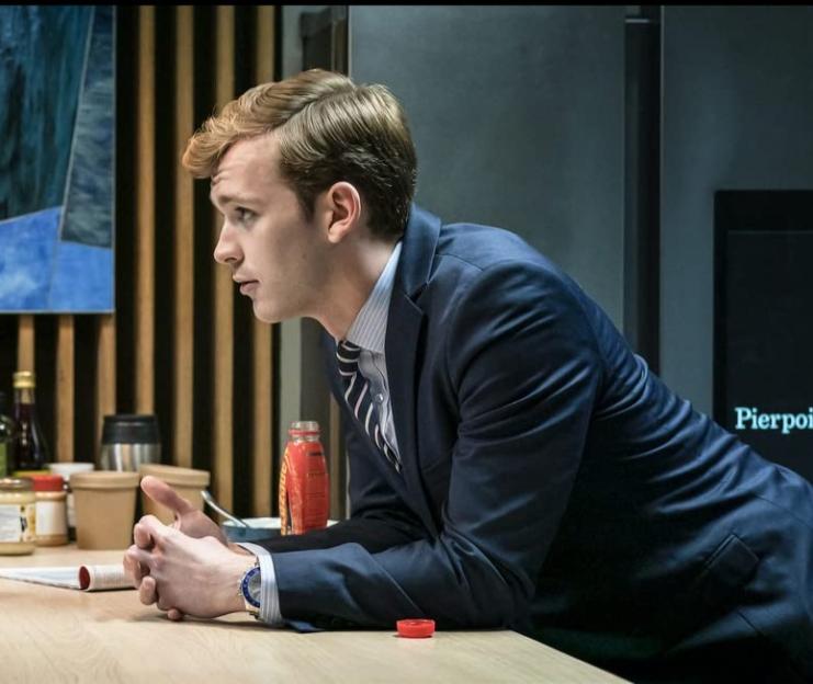 Harry Lawtey in Industry (2020) looking sideways while leaning on a table.