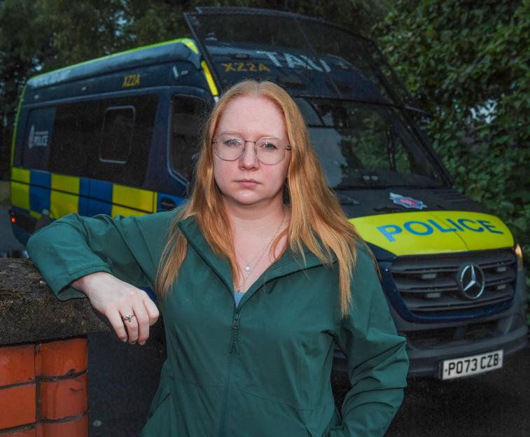 Thea Jacobs, a reporter, stands in front of a police van during early morning drug raid.
