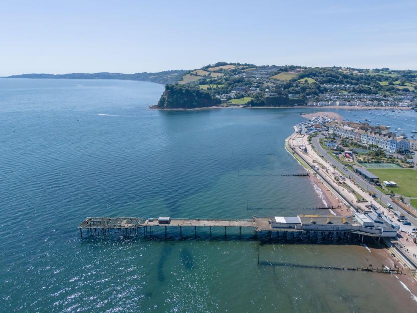 Aerial view of Teignmouth's Half Dilapidated Pier in Devon, showing rotted and missing boards at the end, with the coastline and town in the background.