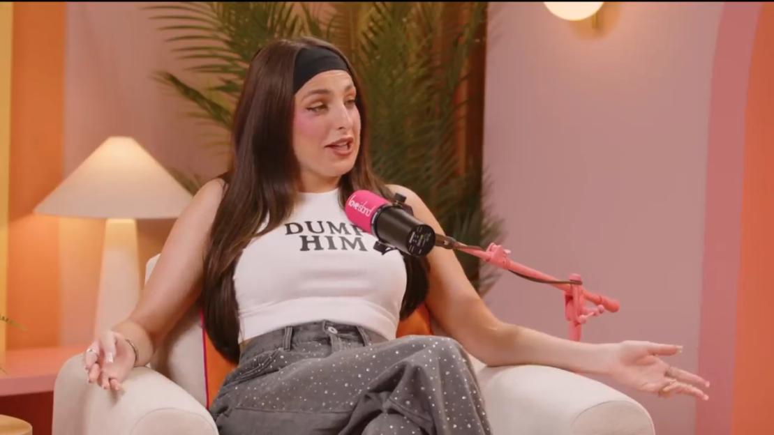 Yasmin Pettet being interviewed on a podcast, wearing a white crop top that says "DUMP HIM".