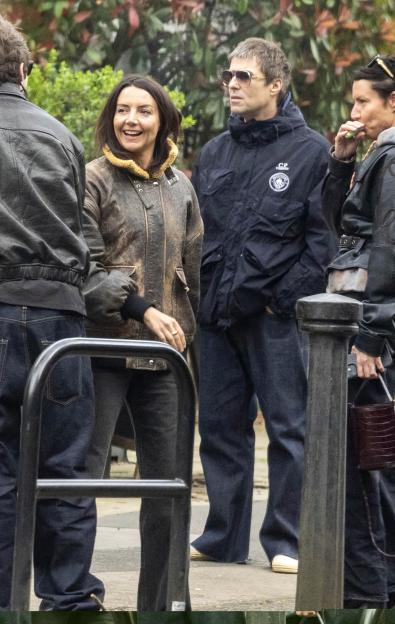 Liam Gallagher and his partner Debbie Gwyther talking in a group outdoors.