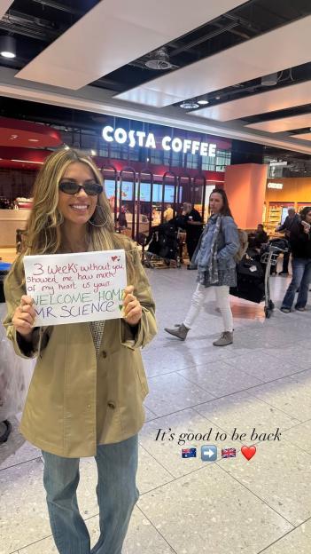 Ekin-Su Cülcüloğlu holding a "Welcome Home Mr. Science" sign at an airport.