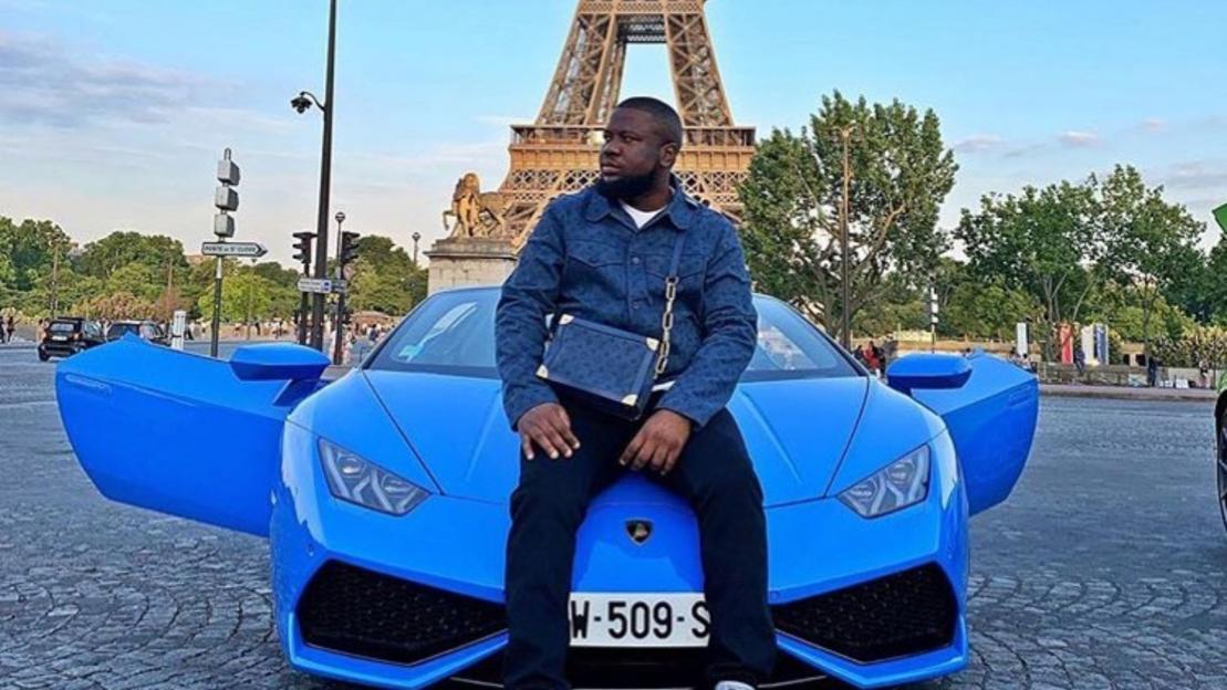 Man sitting on a blue Lamborghini with the Eiffel Tower in the background.