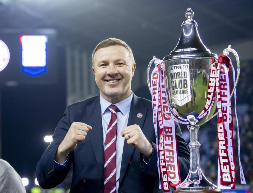 Wigan CEO Kris Radlinski stands next to the Betfred World Club Challenge trophy.