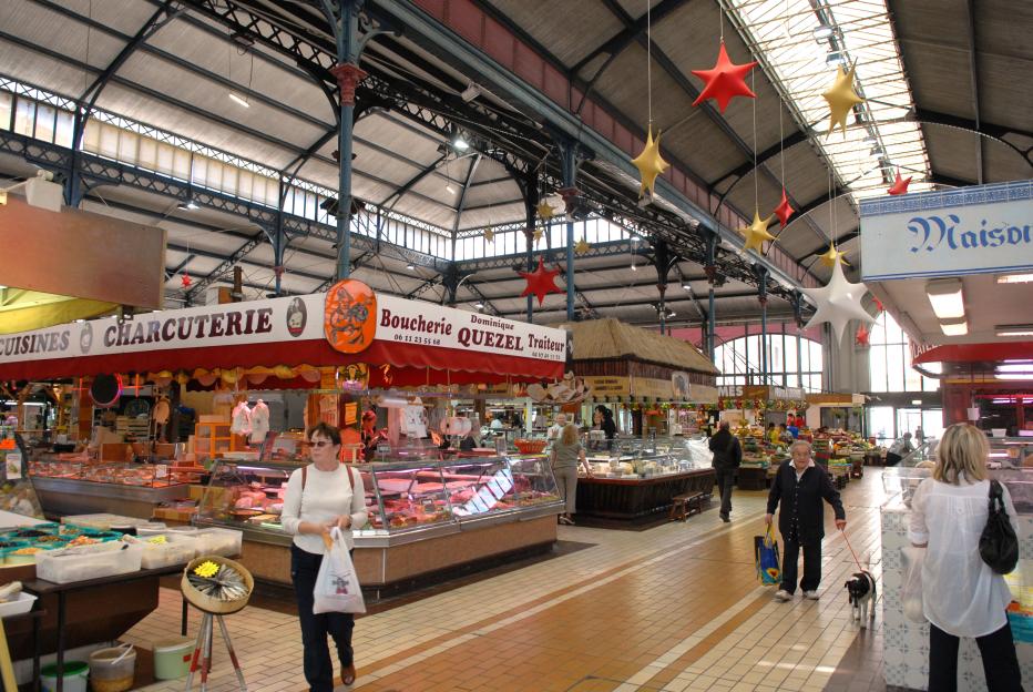 The indoor market at Beziers, France, featuring butcher and charcuterie stalls with people shopping.
