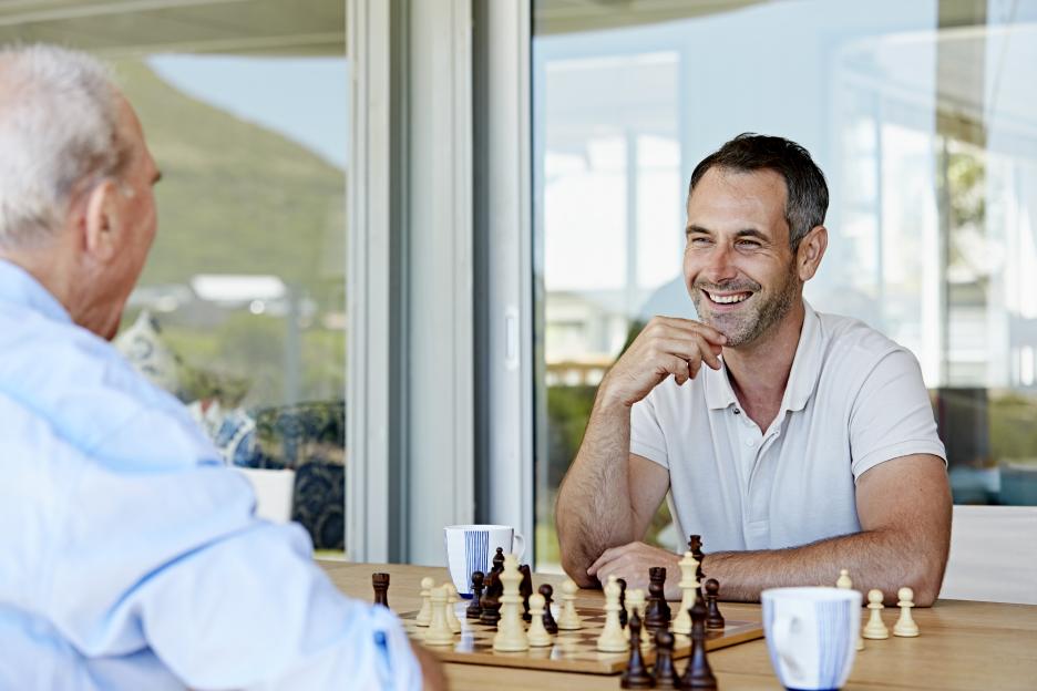 A mature man playing chess with his father on a patio.