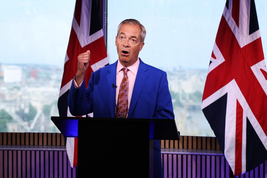 Nigel Farage at a podium with two Union Jack flags behind him.