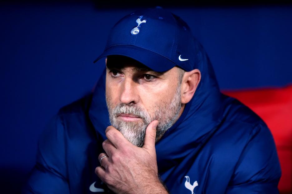 Igor Tudor, wearing a navy blue cap and jacket with the Tottenham Hotspur logo, looks thoughtful with his hand on his chin.