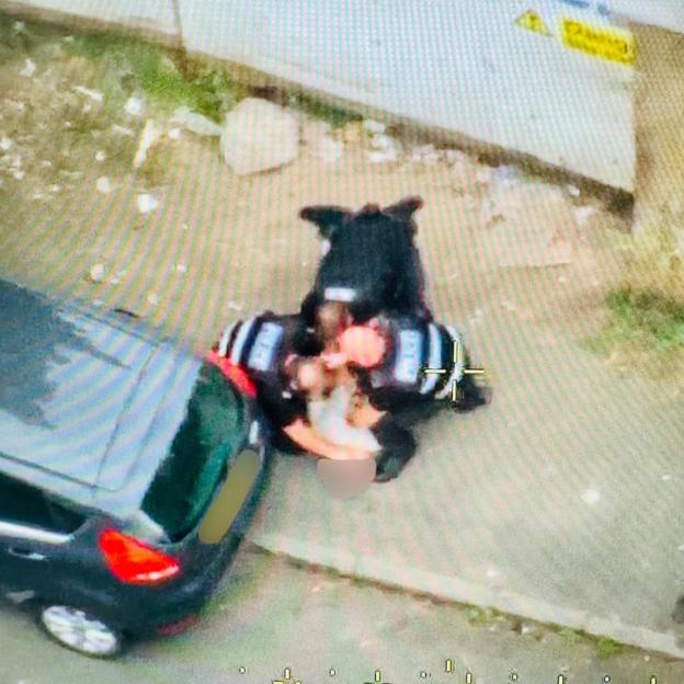 Aerial view of a person in a black jacket and a dark vehicle on a sidewalk.