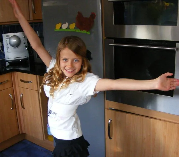 Rachel Catterall’s daughter, Daisy, smiling in a kitchen with her arms outstretched.