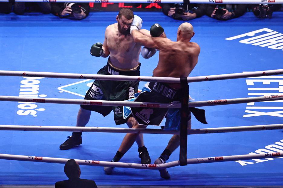 Boxers Tyson Fury and Arslanbek Makhmudov exchange punches in the boxing ring.