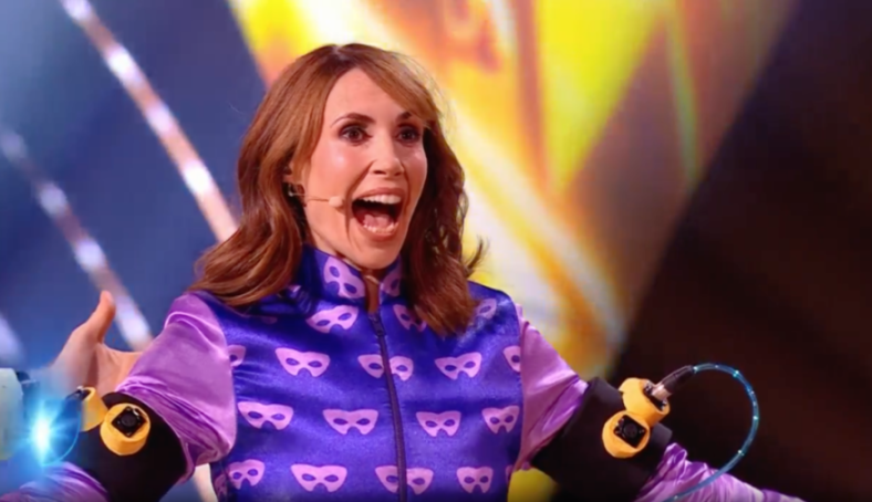 Woman in a purple jacket with face mask patterns and arm attachments, looking surprised.