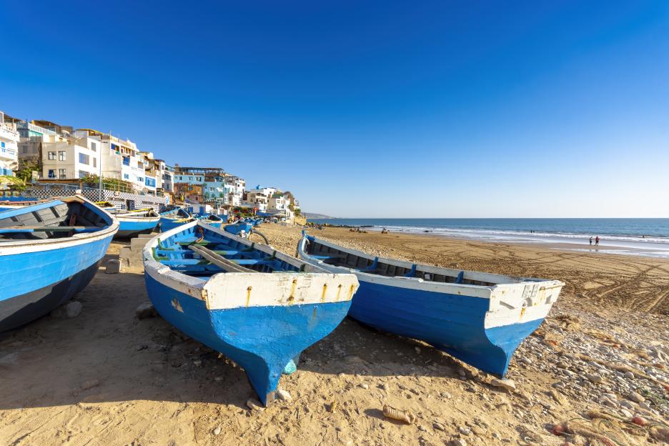 Fishing boats on the beach at Taghazout, Morocco, with the town and ocean in the background.