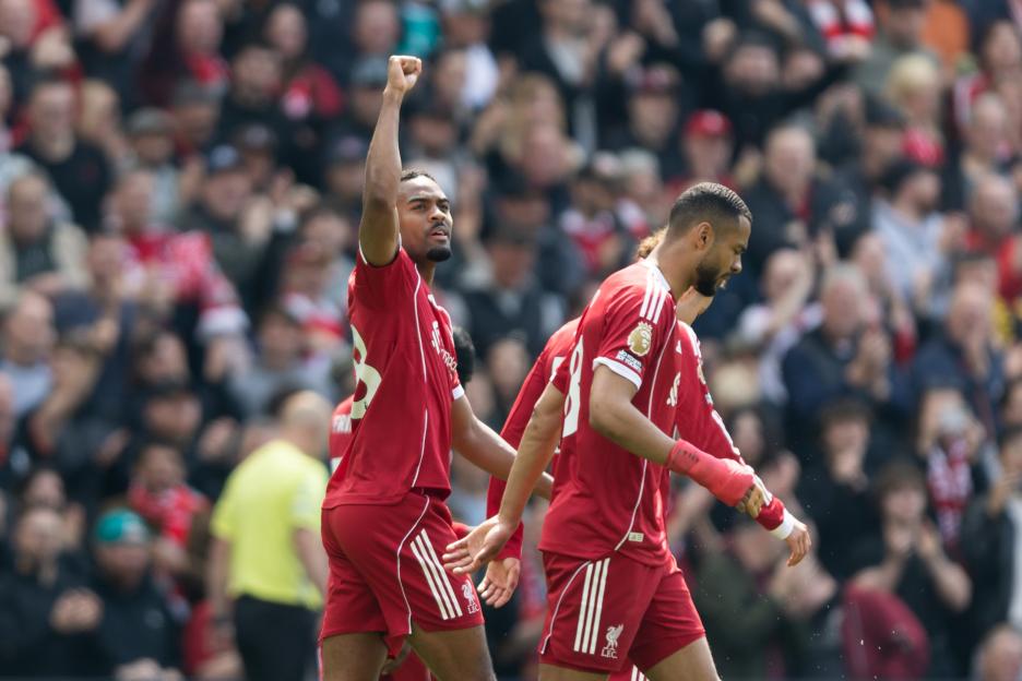 Liverpool player celebrating a goal with his fist raised, another player with a bandaged arm walks beside him.