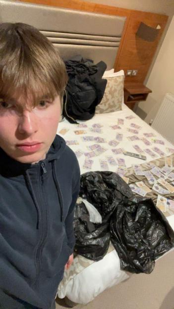 Johannes Natland stands next to a bed covered in money.