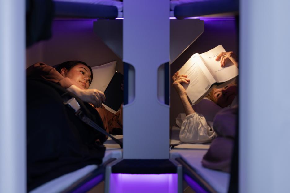 Two people relax in bunk beds on an airplane, with purple ambient lighting.